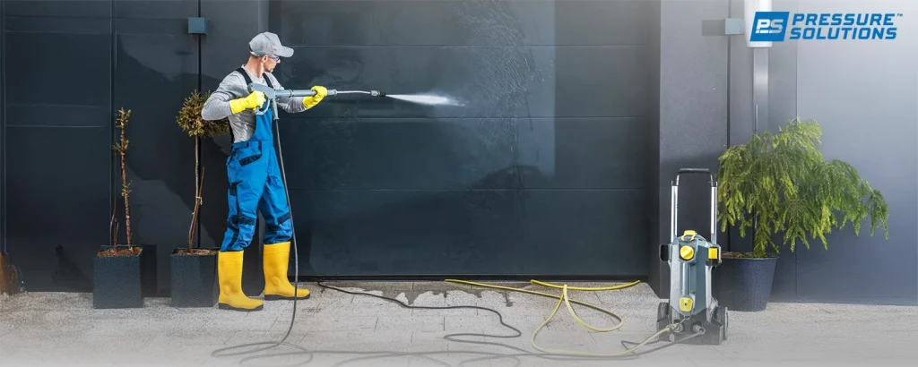 A professional operator using a petrol water blaster to clean a dark grey exterior wall, illustrating the practical application of the equipment discussed in this guide on choosing the best unit.