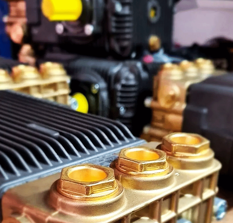 Maintenance schedule final A close-up, detailed photograph of high-pressure water blaster pumps, focusing on the golden brass manifold and components.